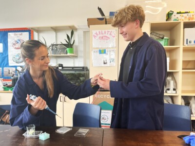 a male and female student in blue lab coats take a sample