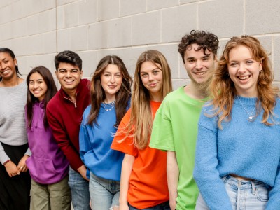 Students standing against grey wall with bright jumpers on