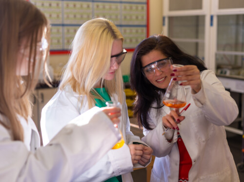 Female chemistry students in lab coats looking at a test tube with their teacher