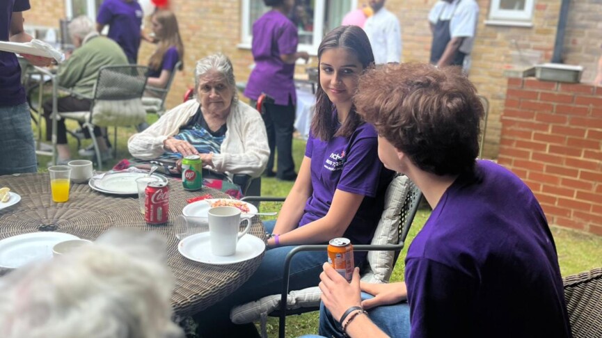 Health and Social Care students wearing purple polo shirts talk to residents in a care home