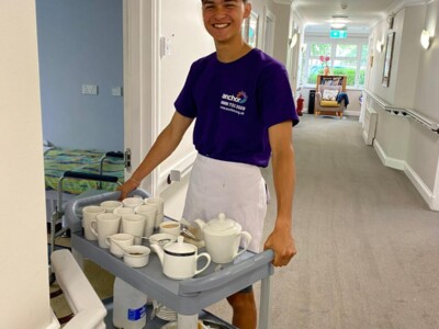 male student delivering tea tray to residents in a care home