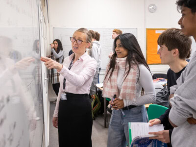 Female maths teacher helping some students with an equation on the whiteboard