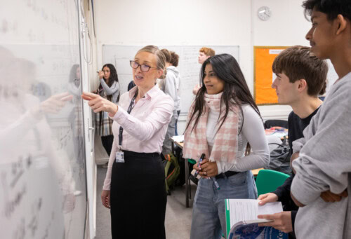 Female maths teacher helping some students with an equation on the whiteboard