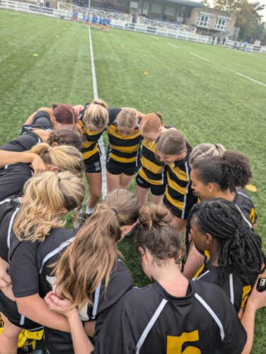 Women's Rugby team in a group huddle on the pitch