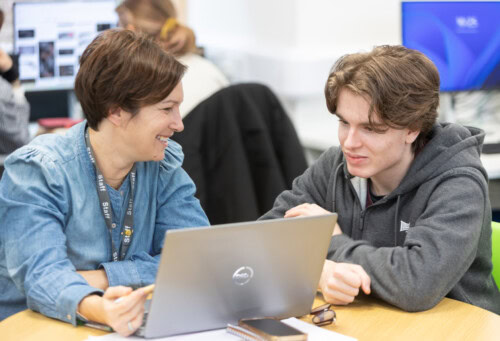 A female learning support assistant helping a male student at the computer