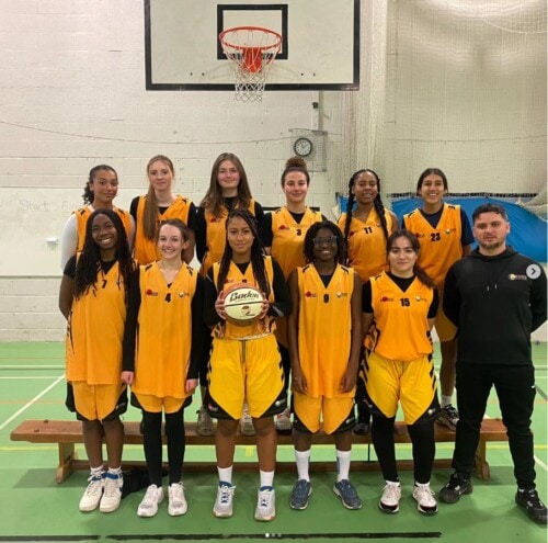 Women's Basketball team posing for a team photo underneath the hoop