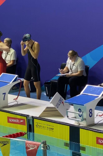 A competitive swimmer in a blue costume adjusting goggles and about to start a race