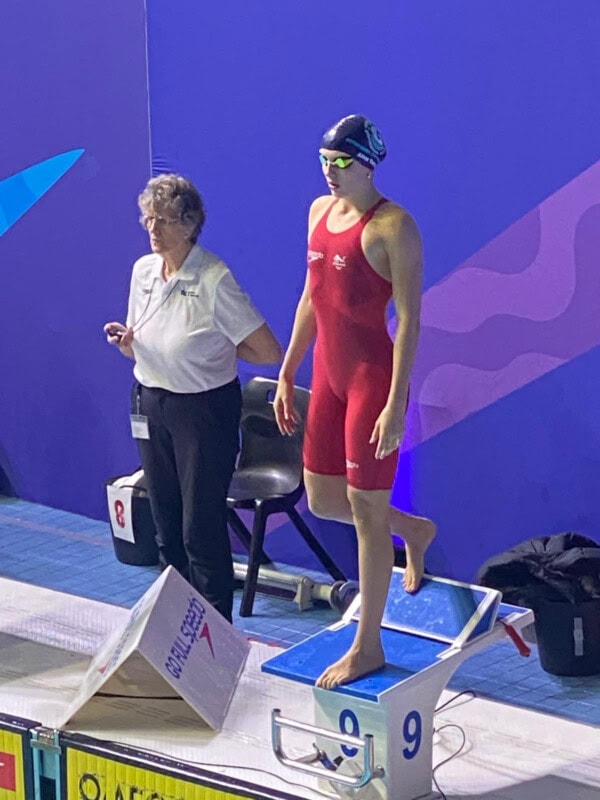 Swimmer in a red costume at the podium about to dive into pool