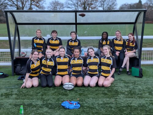 women's rugby team sitting together in their kit under a shelter