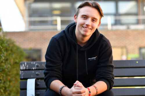 Male student wearing a black hoodie sitting gently forward and smiling