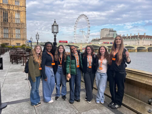 Group of female students posing by Thames with London Eye in the bakground